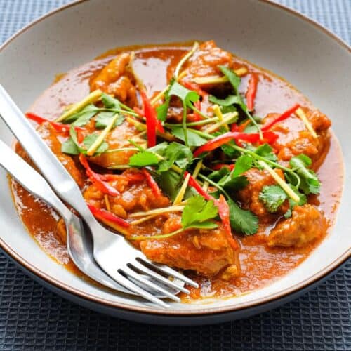 A bowl of Burmese chicken curry with fork and spoon