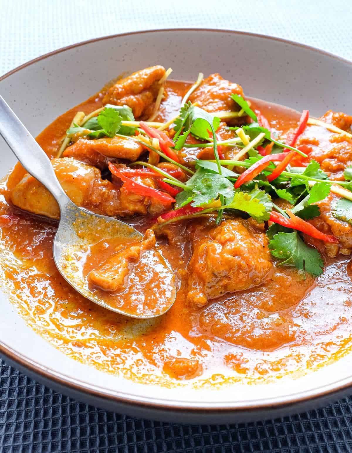 A bowl of Burmese chicken curry with spoon