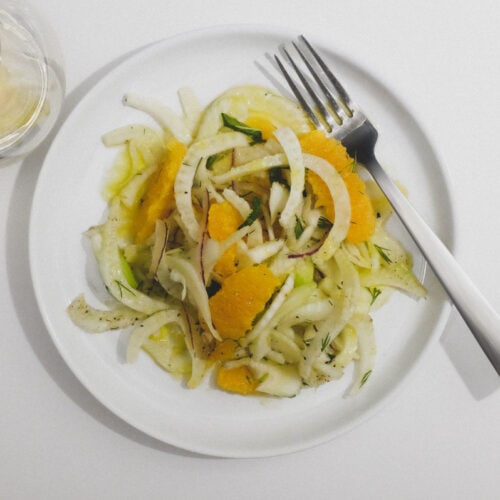 A plate of fennel & Orange Salad with a glass of white wine to the side.