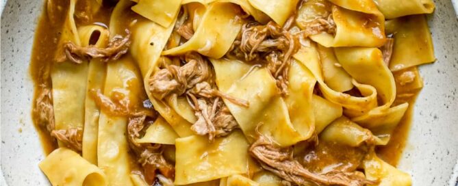 A bowl of pappardelle pasta with a lamb ragu sauce on a blue tea towel background