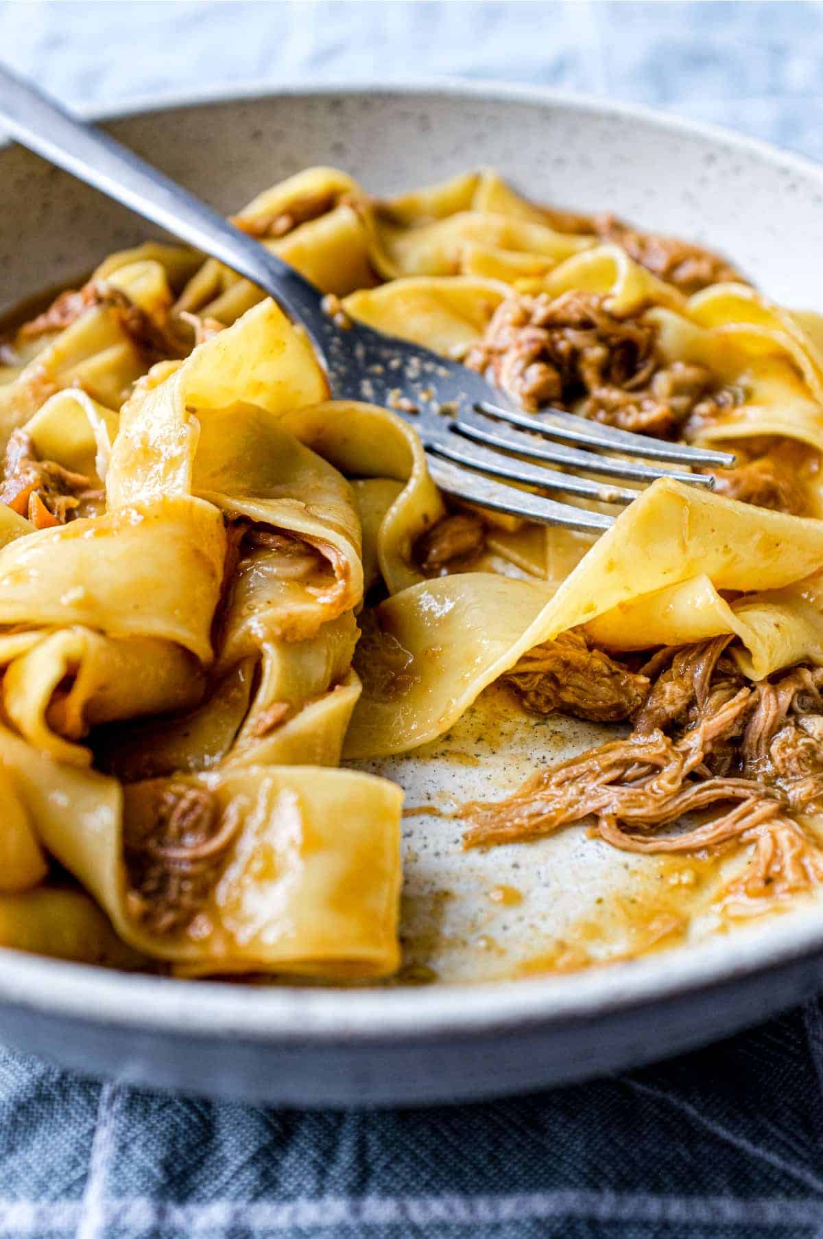 A bowl of pappardelle pasta with a lamb ragu sauce with a fork