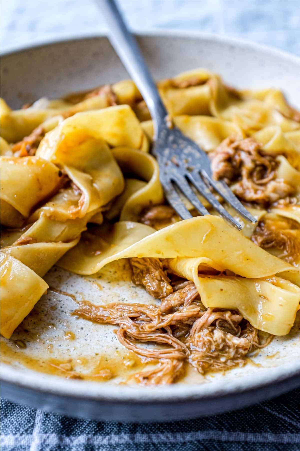 A bowl of pappardelle pasta with a lamb ragu sauce with a fork