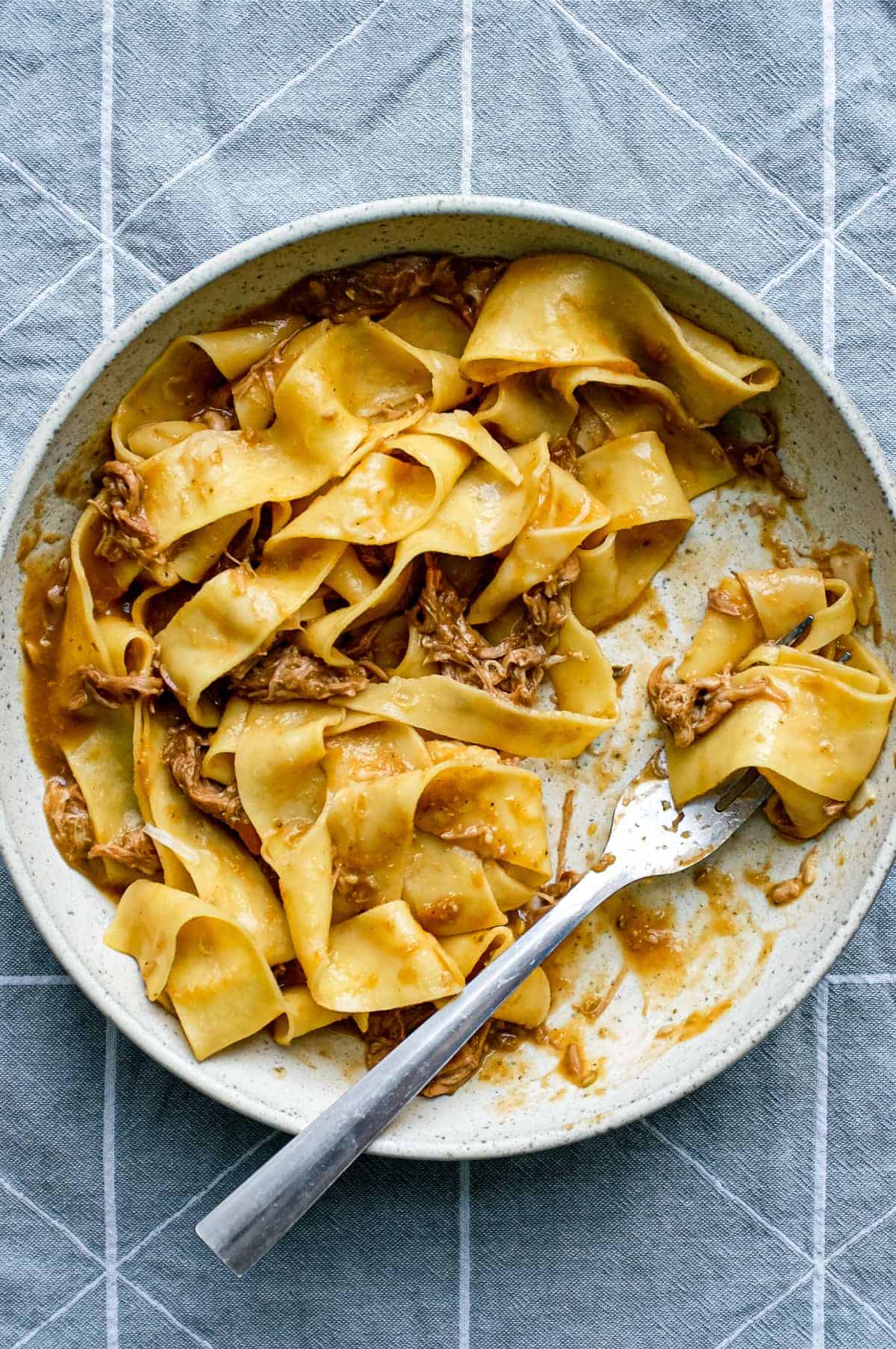 A bowl of pappardelle pasta with a lamb ragu sauce with a fork