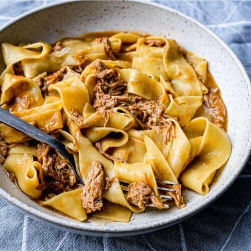 A bowl of pappardelle pasta with a lamb ragu sauce with a fork