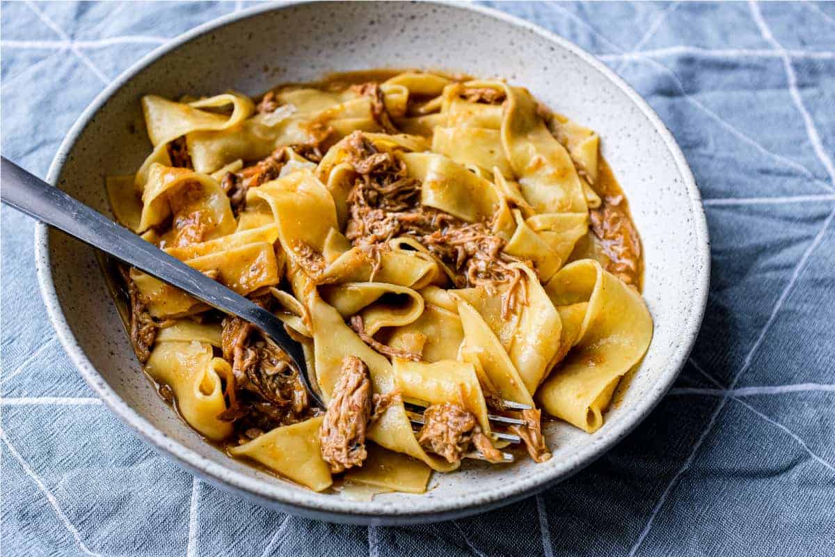 A bowl of pappardelle pasta with a lamb ragu sauce with a fork