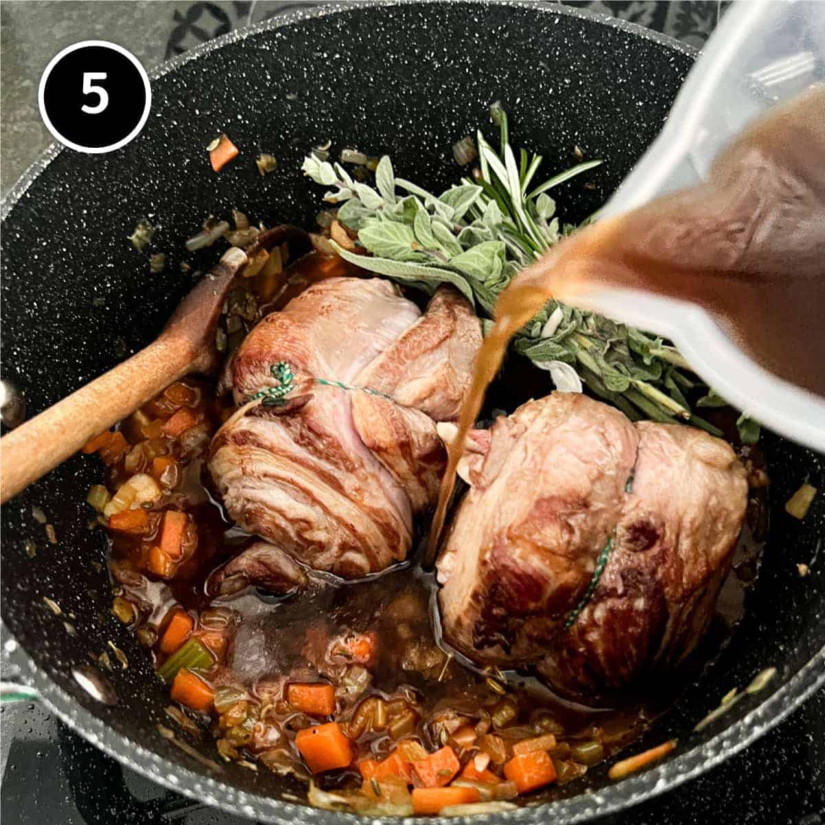 Pouring beef tock into a pan with lamb, vegetables and herbs.