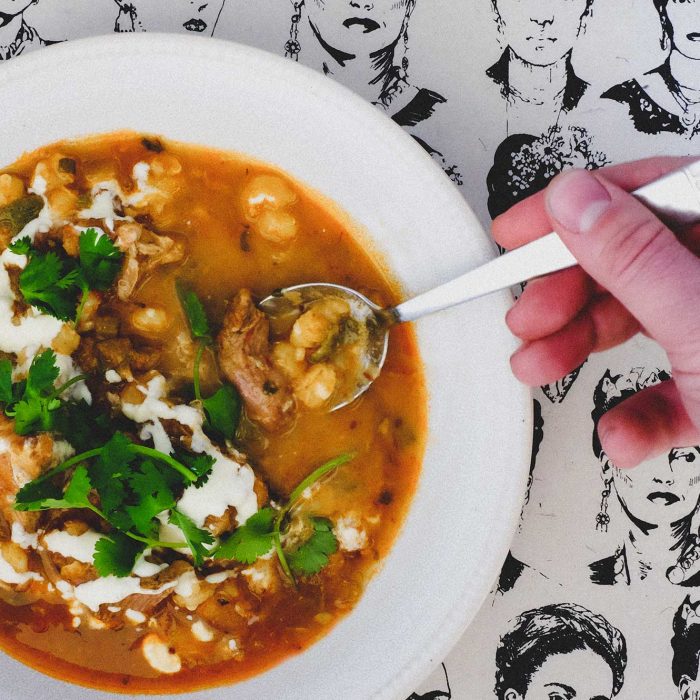 A bowl of Mexican Pozole Rojo on a background featuring sketches of Frida Kahlo