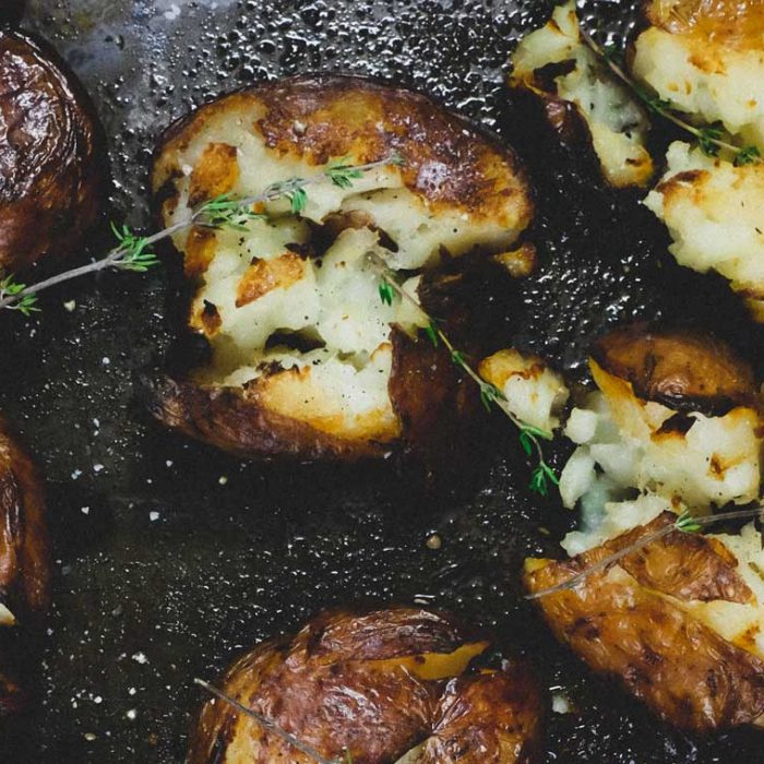 Punched potatoes on a baking sheet garnished with a little fresh thyme.