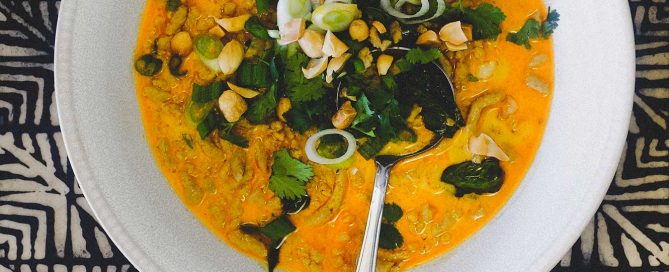 A bowl of Thai yellow curry with minced pork. Surrounding the bowl are smaller bowls of spring onions, cilantro, peanuts and jasmine rice.