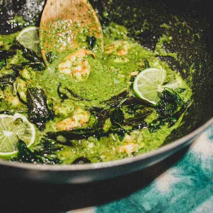 A pan of green masala with shrimp scattered with fried curry leaves and lime slices