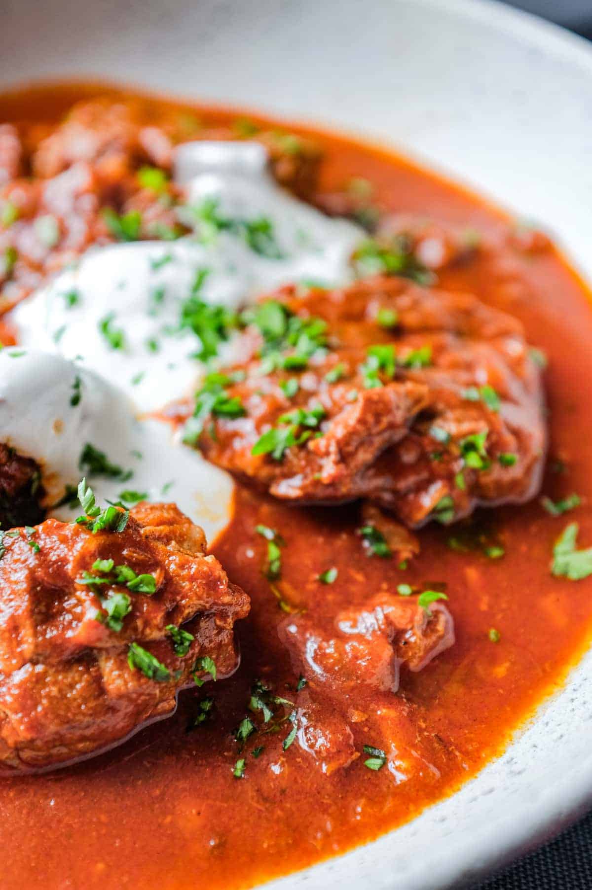 A plate of Hungarian Pörkölt Beef Stew drizzled with sour cream and garnished with parsley