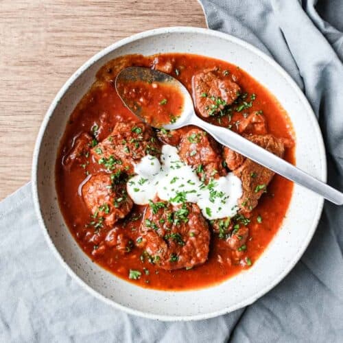 A bowl of Hungarian Pörkölt Beef Stew in a bowl, wrapped in a tea towel.