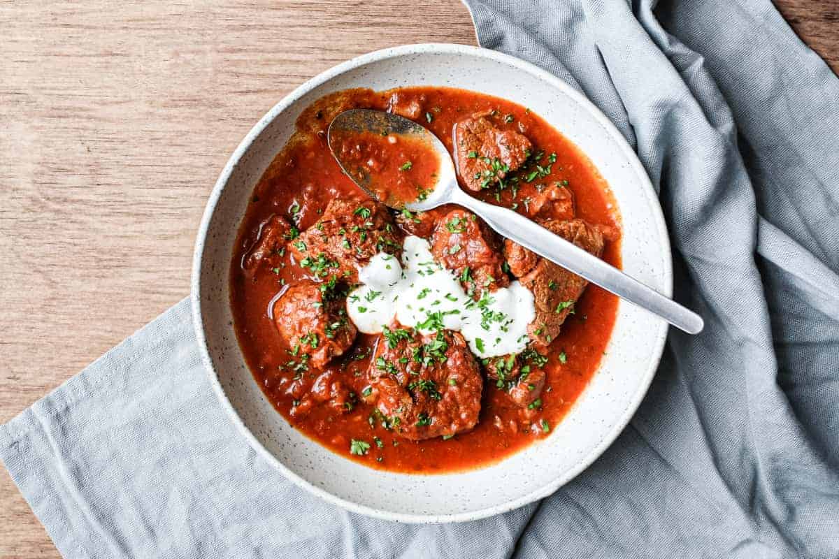 A bowl of Hungarian Pörkölt Beef Stew in a bowl, wrapped in a tea towel.