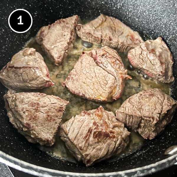 Beef being browned in a large pot with butter.