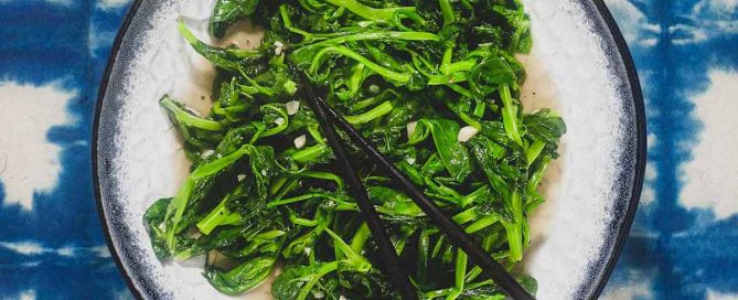 A platter of stir fried sno pea shoots on a blue batik background