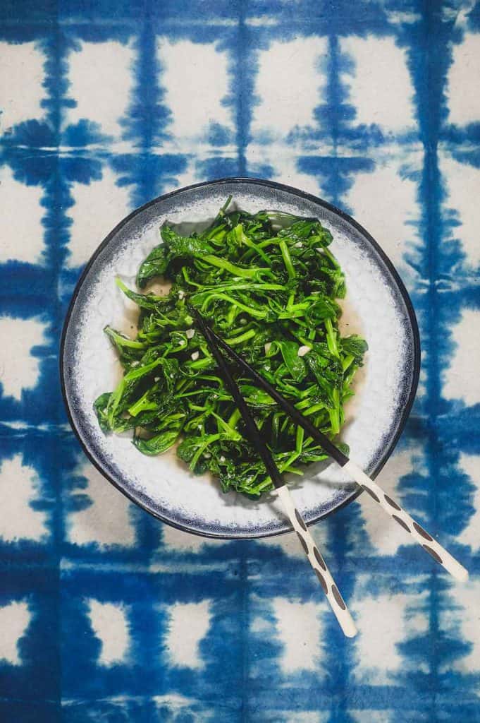 A platter of stir fried sno pea shoots on a blue batik background