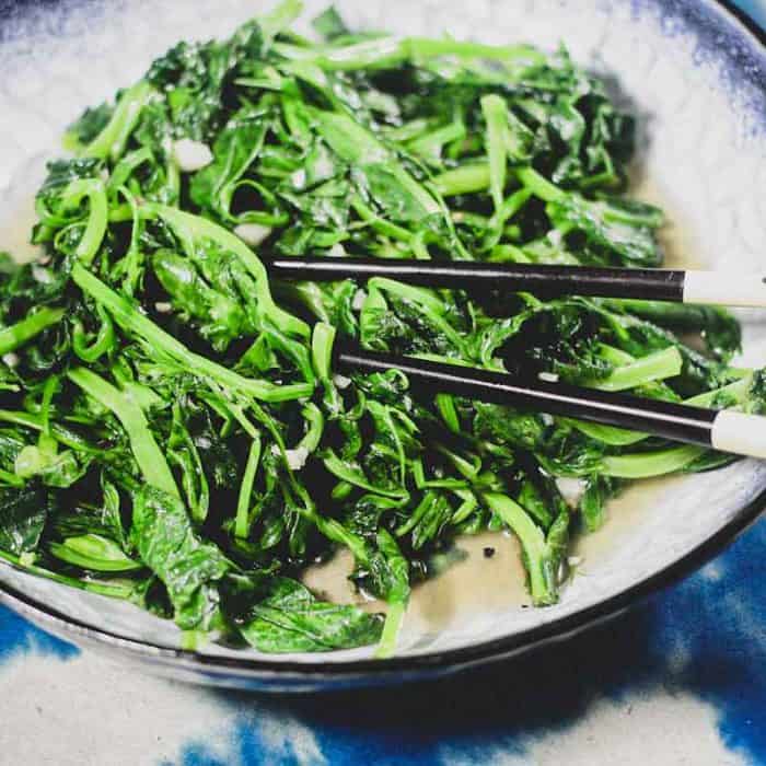 A platter of stir fried sno pea shoots on a blue batik background