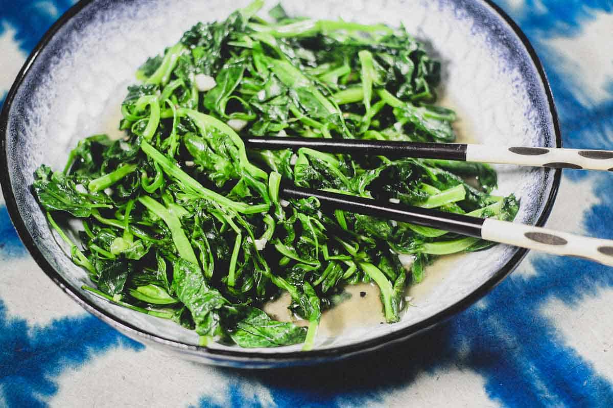 A platter of stir fried sno pea shoots on a blue batik background