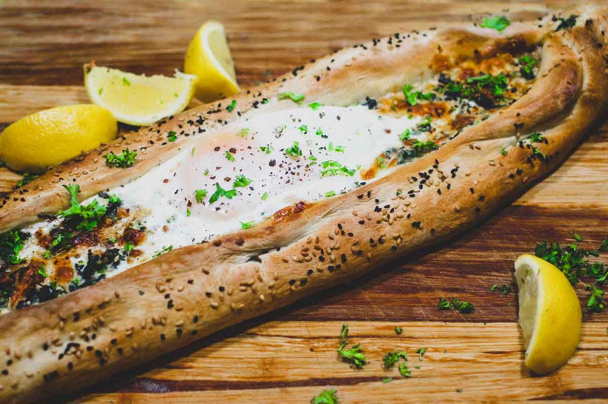 A whole Turkish Cheese, Egg & Spinach Pide on a wooden board