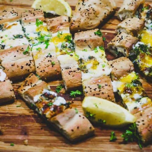 A sliced Turkish Cheese, Egg & Spinach Pide on a wooden board