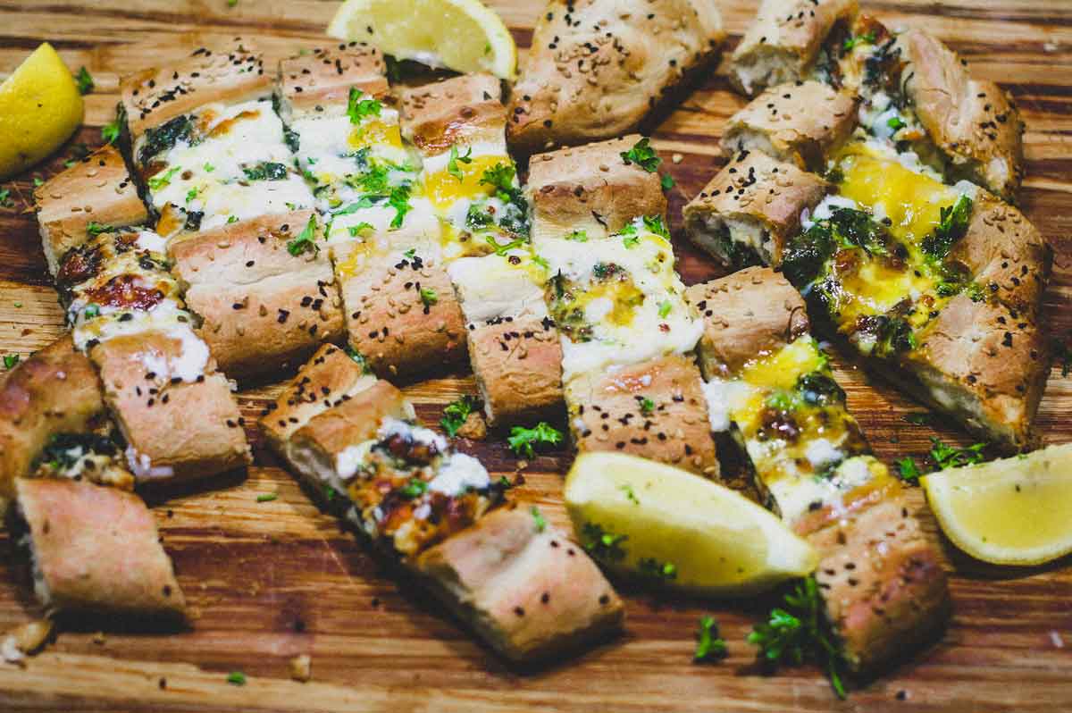 A sliced Turkish Cheese, Egg & Spinach Pide on a wooden board