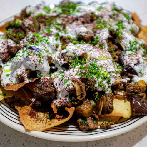 a platter of Lamb & Eggplant Fatteh garnished with fresh parsley and sumac