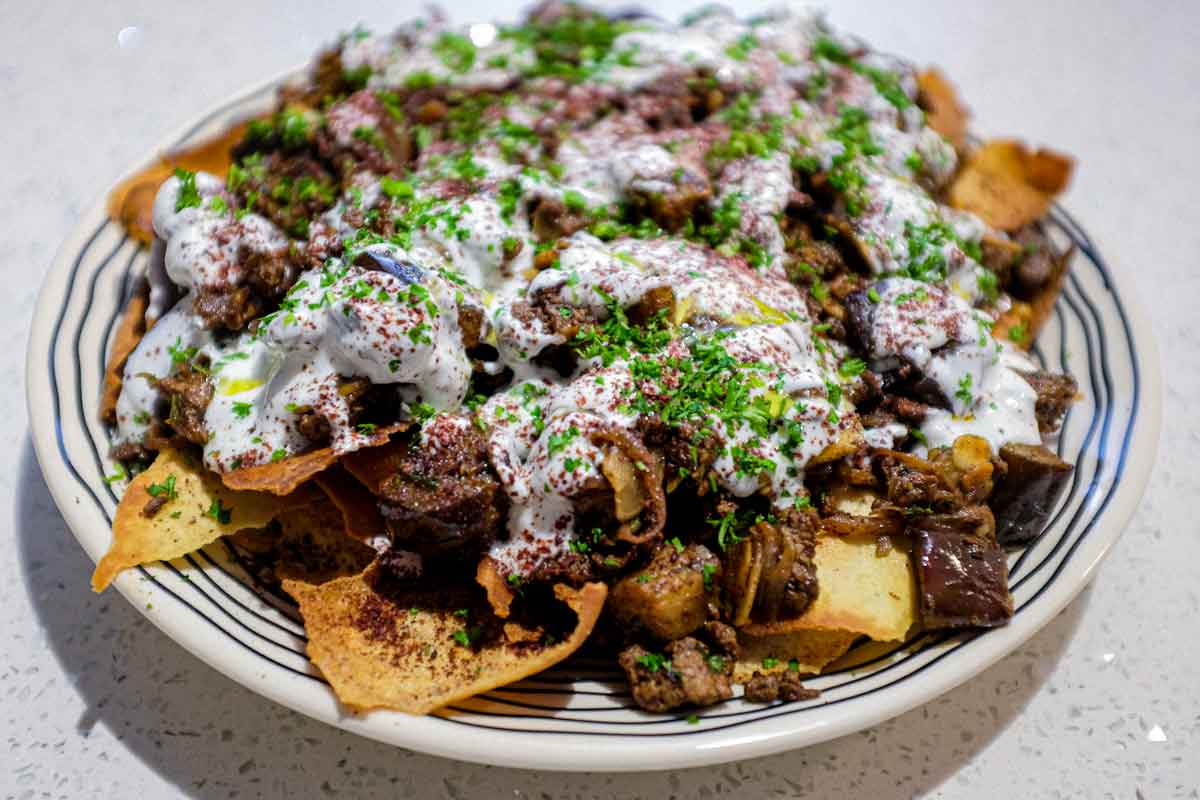 a platter of Lamb & Eggplant Fatteh garnished with fresh parsley and sumac