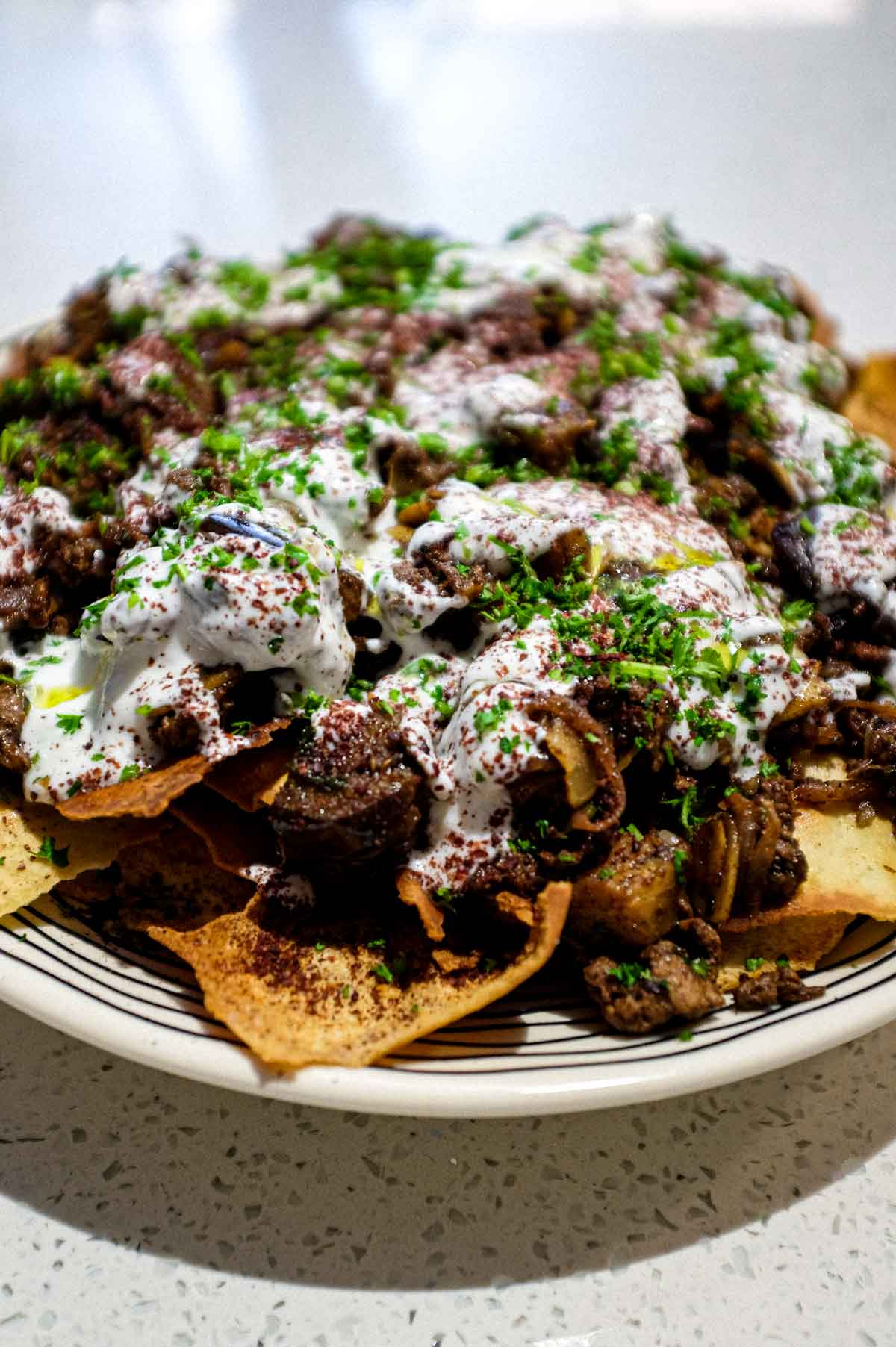 a platter of Lamb & Eggplant Fatteh garnished with fresh parsley and sumac