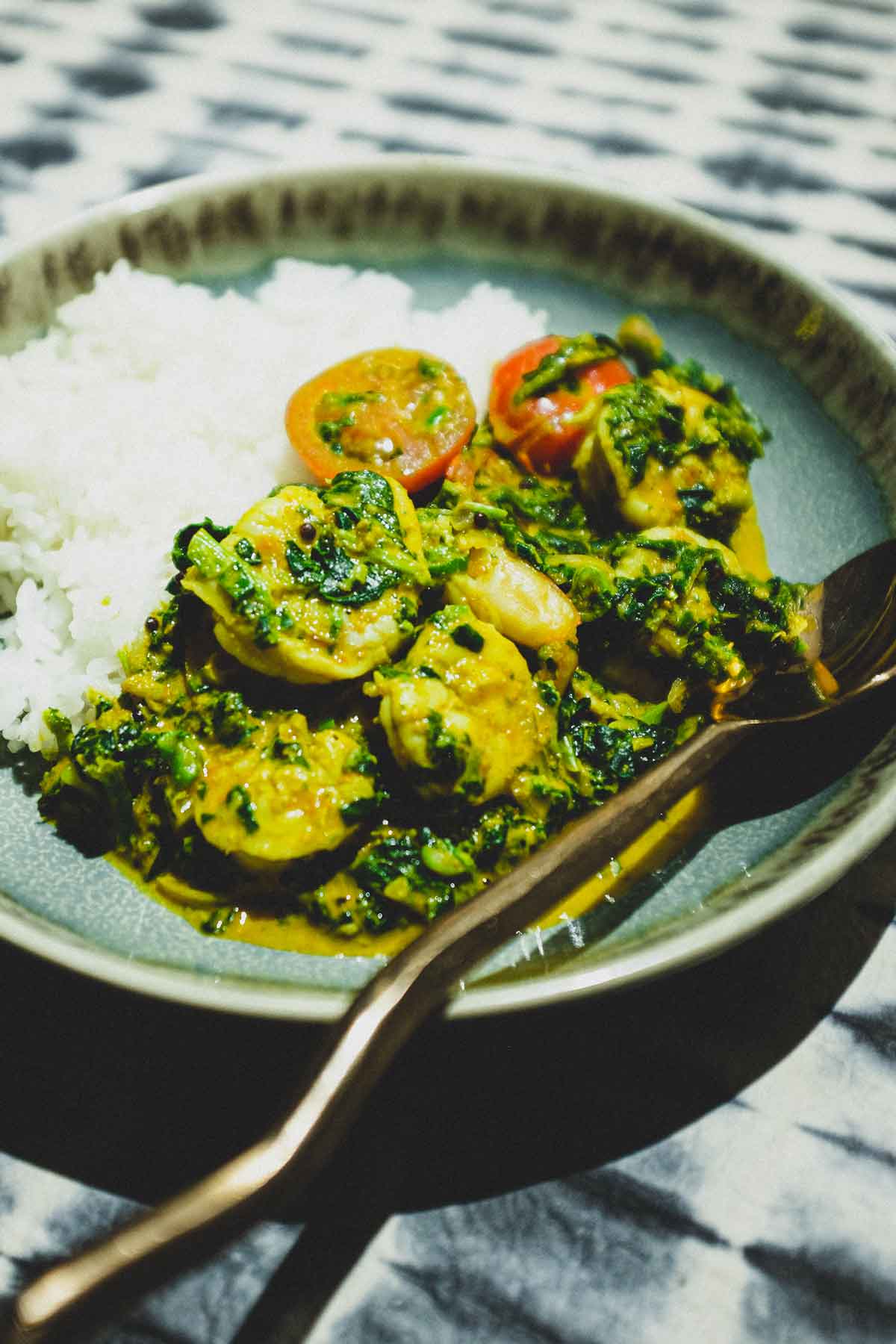 A small bowl of shrimp curry and rice with a fork and spoon