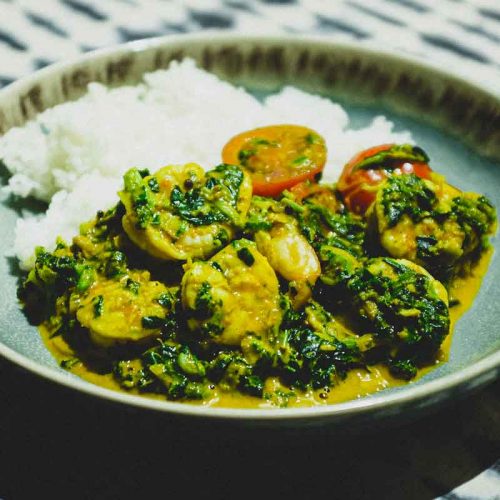 A small bowl of shrimp curry and rice with a fork and spoon