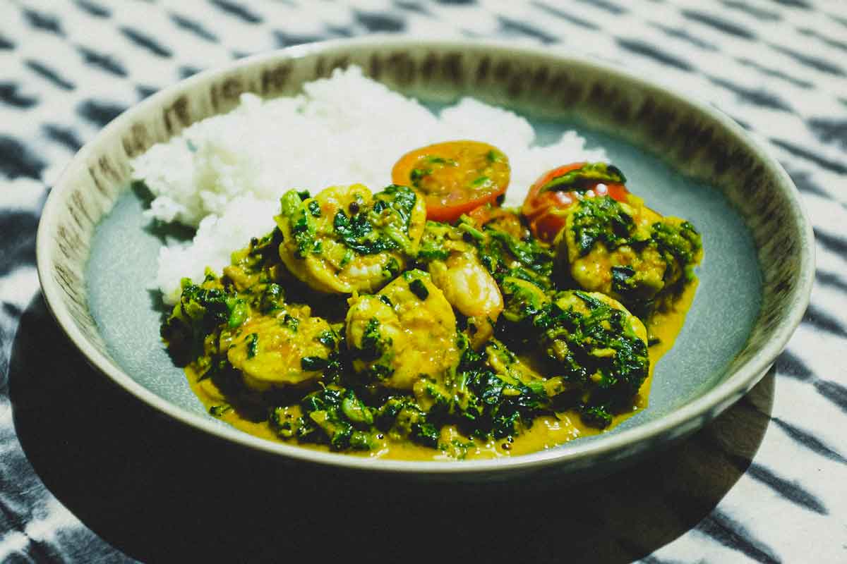 A small bowl of shrimp curry and rice with a fork and spoon