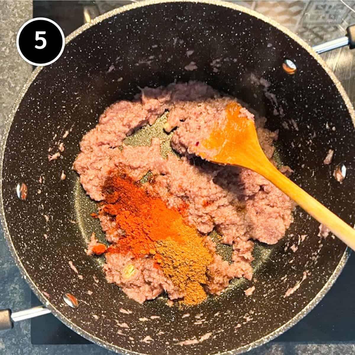 Spices being added to fried onion pureeing a pan with a wooden spoon