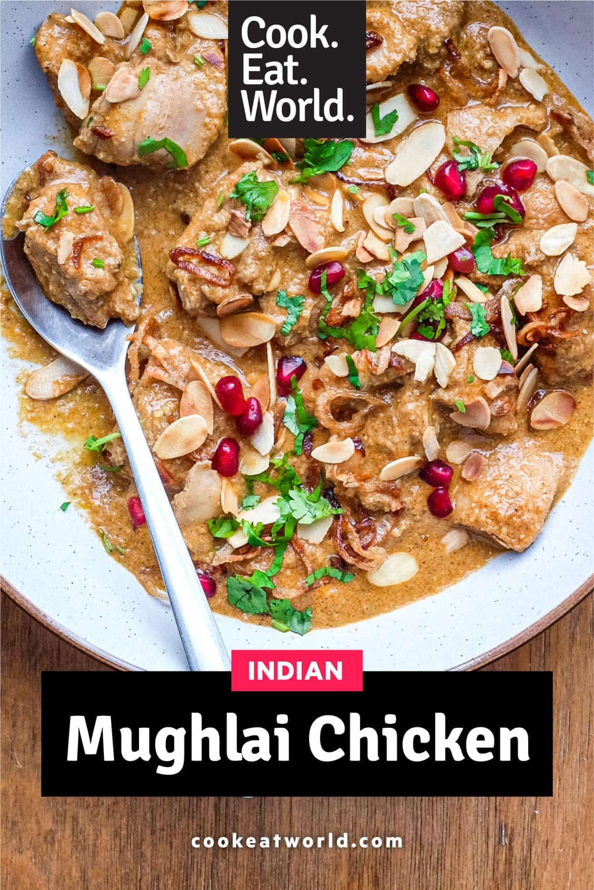 A bowl of Mughlai Chicken Curry garnished with Almonds, cilantro and pomegranate seeds with a spoon on the side.