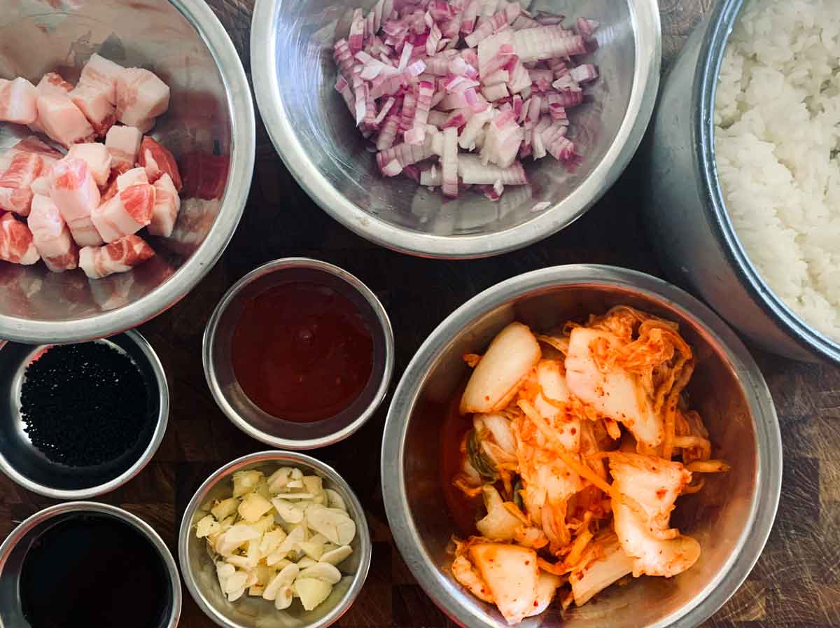 The ingredients for kimchi fried rice: kimchi, rice, onion, bacon, gochujang, garlc, soy and rice.
