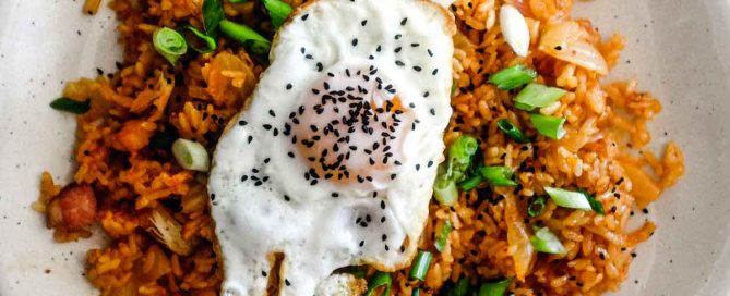A plate of kimchi fried rice with a crisp fried egg on top scattered with spring onions