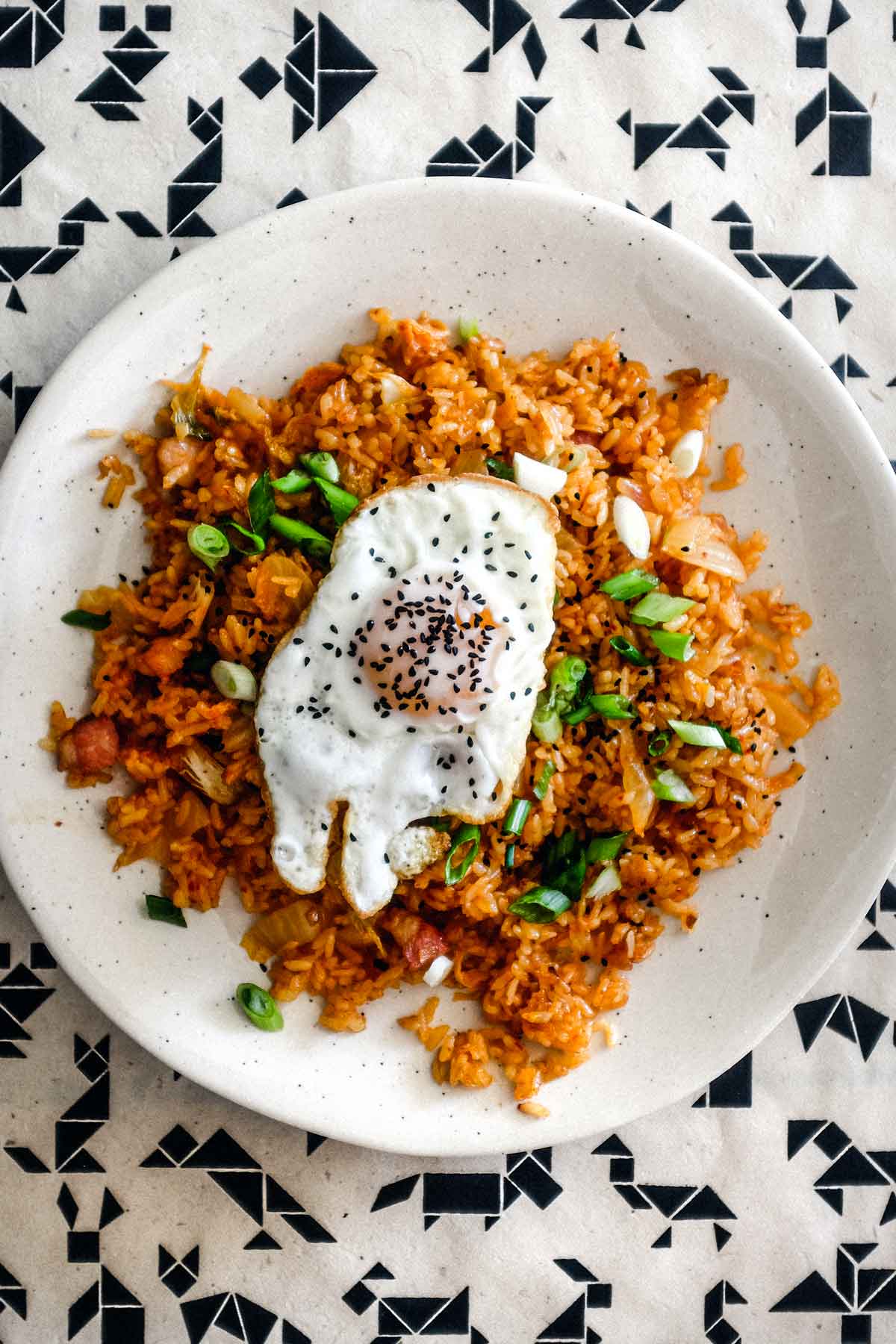 A plate of kimchi fried rice with a crisp fried egg on top scattered with spring onions