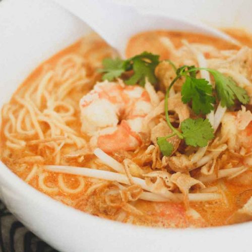 A bowl of Malaysian curry laksa decorated with prawns, tofu , beansprouts and herbs