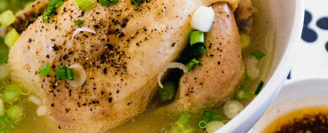 A bowl of Korean Samgyetang Soup with whole Cornish hen. A dipping sauce sits beside the bowl.