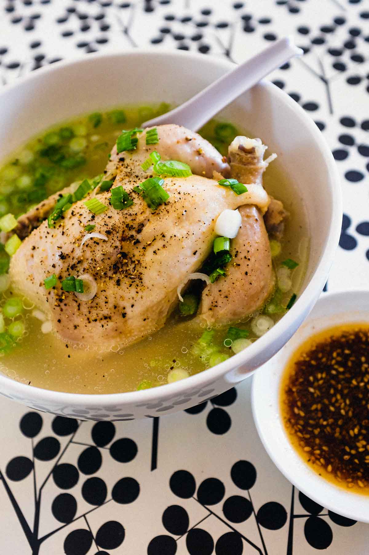 A bowl of Korean Samgyetang Soup with whole Cornish hen. A dipping sauce sits beside the bowl.