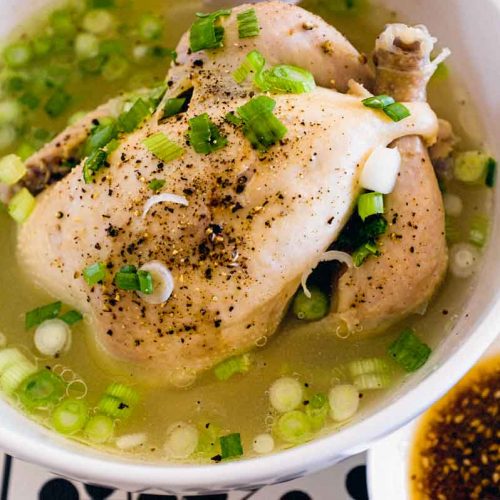 A bowl of Korean Samgyetang Soup with whole Cornish hen. A dipping sauce sits beside the bowl.