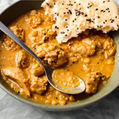 A bowl of lentil curry with a spoon and piece of naan bread