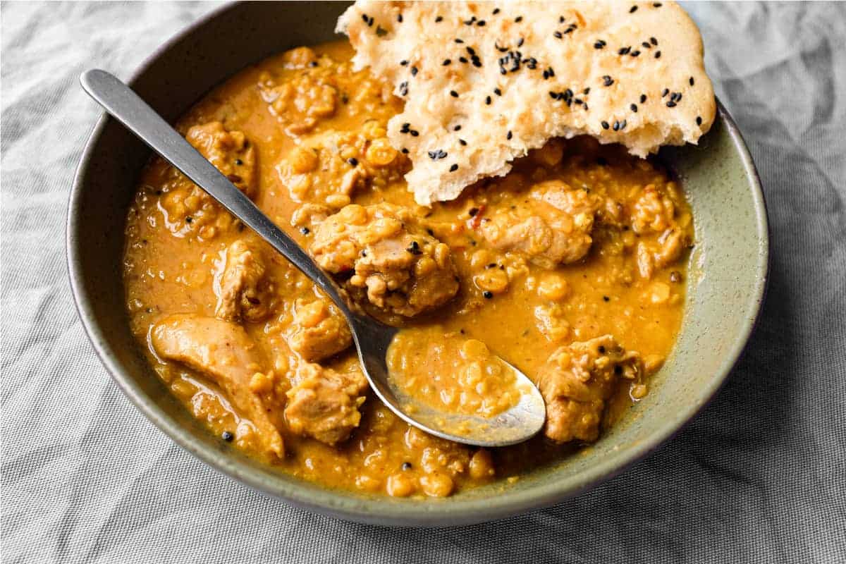 A bowl of lentil curry with a spoon and piece of naan bread