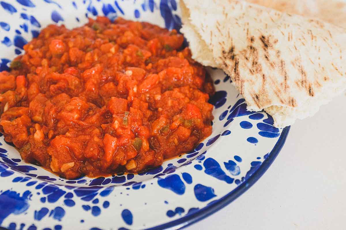 Moroccan Matbucha in a vibrant blue meze bowl. Peppers and tomatoes are stewed to a thick, tangy paste.