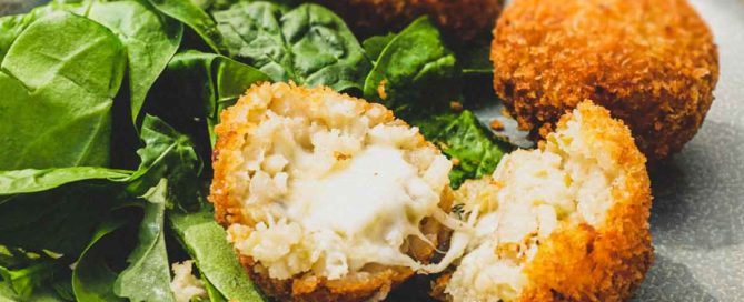 Suppli (Italian Rice Balls) on a plate with some fresh spinach leaves