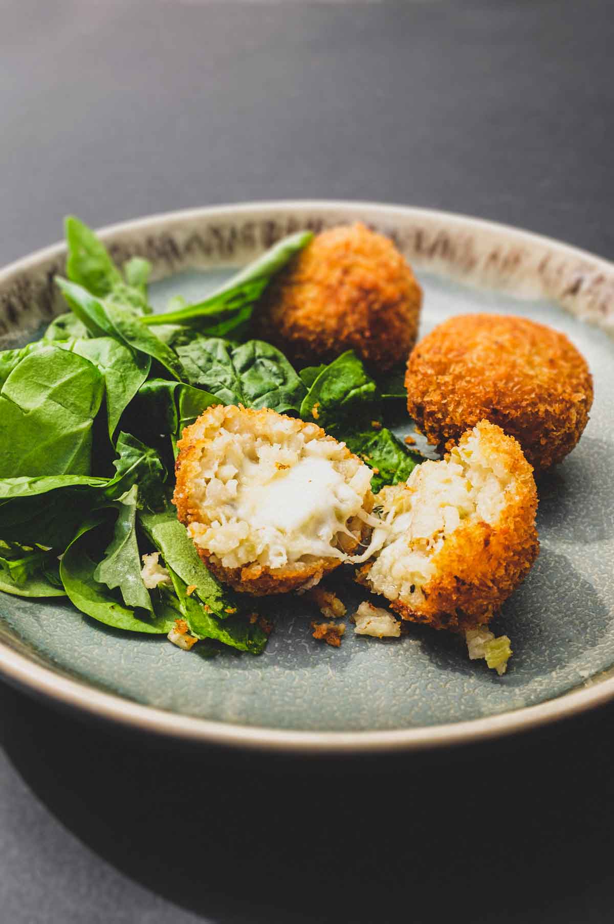 Suppli (Italian Rice Balls) on a plate with some fresh spinach leaves