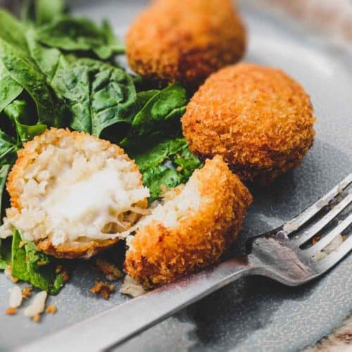 Suppli (Italian Rice Balls) on a plate with some fresh spinach leaves