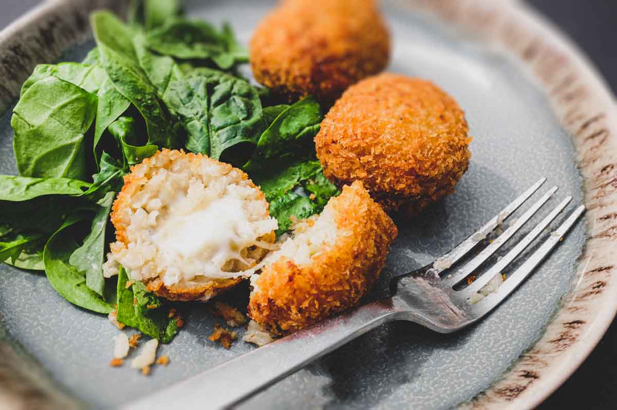 Suppli (Italian Rice Balls) on a plate with some fresh spinach leaves