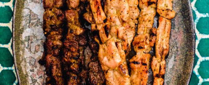 Beef and Pork satay skewers sit on a serving platter on a green batik background.
