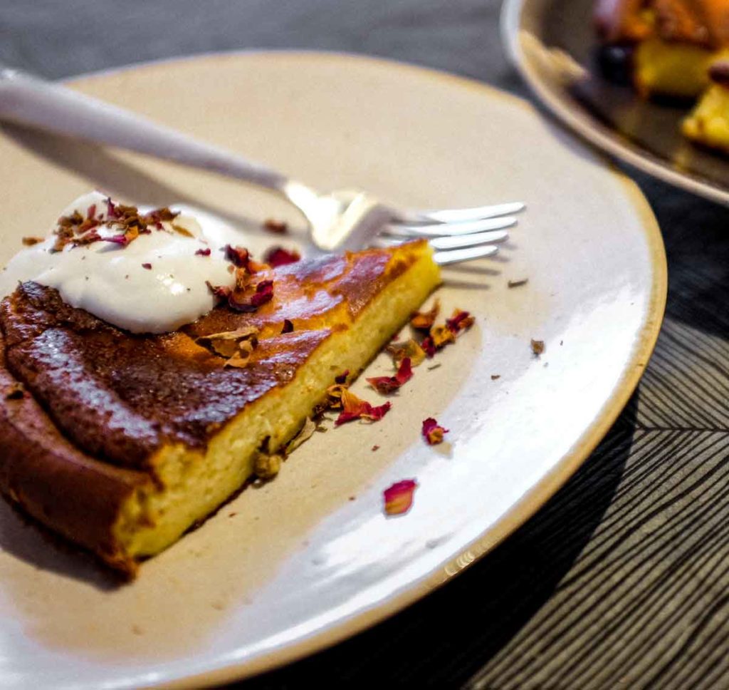 Turkish Lime Yoghurt Cake on a plate with cream, scattered with rose petals.