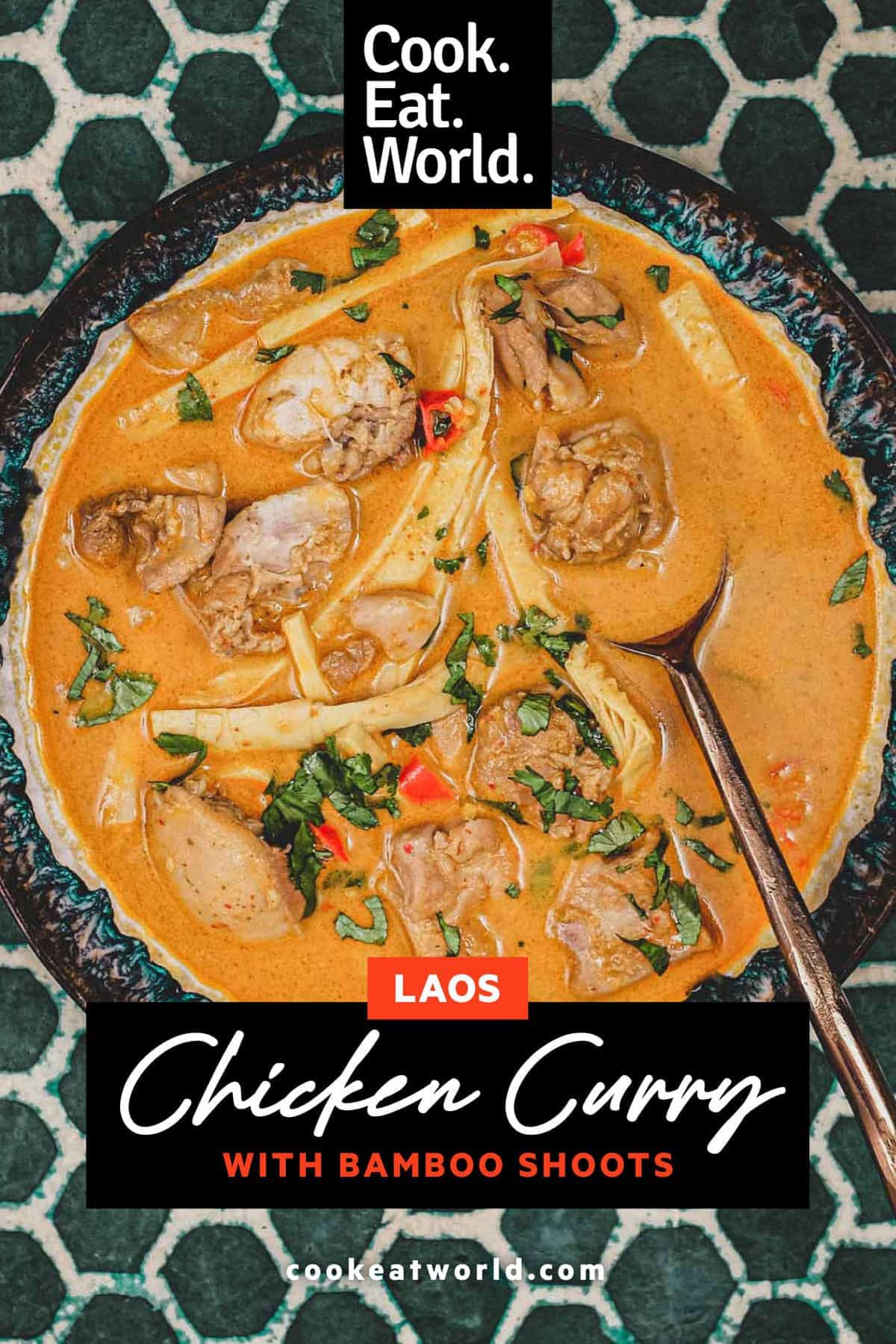 A bowl of vibrant orange Laotian chicken curry and spoon on a green batik background 